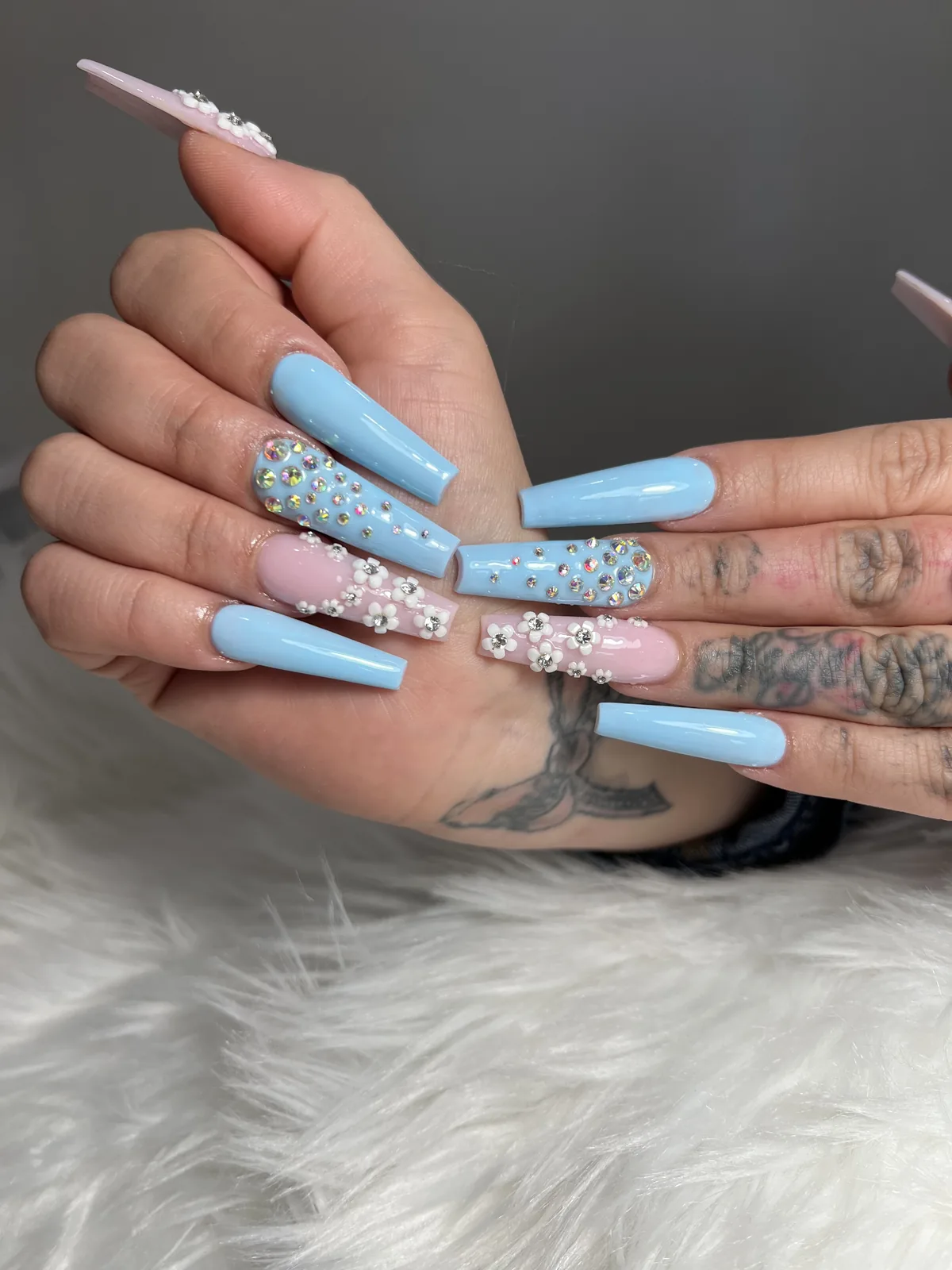 Long sky-blue coffin nails with iridescent rhinestone clusters and 3D white flowers